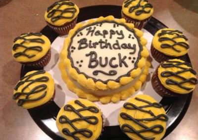 A cake surrounded by yellow cupcakes. The image showcases a cake in the center, with several yellow cupcakes arranged around it