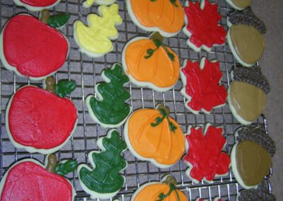 Low-sugar cookies shaped like apples, leaves, pumpkins, red leaves, and coconuts. The cookies are designed in various autumn-themed shapes, perfect for a healthier treat during the fall season