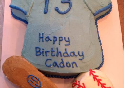A custom birthday cake designed to look like a shirt, bat, and ball for a kid's birthday celebration