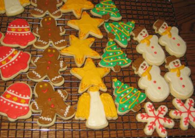 Christmas-themed cookies shaped like bells, snowmen, stars, trees, snowflakes, and gingerbread men. The cookies are decorated with festive designs, perfect for adding a touch of holiday cheer to any celebration
