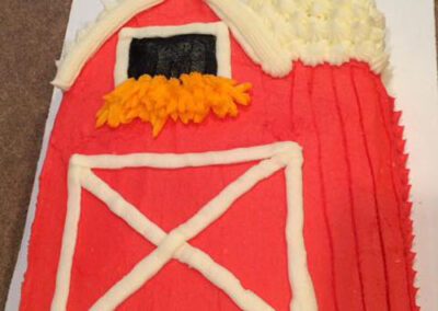 A house-shaped cake with a white roof, red walls, and a green base. The cake is designed to resemble a charming little house, with each element of the cake representing different parts of a house